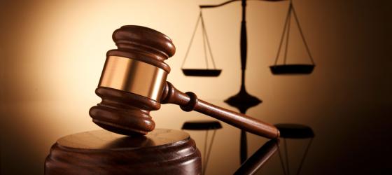 immagine primo piano di un martello in legno e sullo sfondo una bilancia a due braccia simboli della giustizia