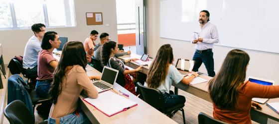 foto studenti seduti in aula con docente in piedi che spiega