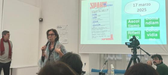 aula universitaria, sullo sfondo schermo con data e titolo ebento, una docente in primo piano parla al microfono all'aula