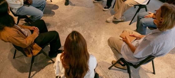 gruppo persone adulte e uomini e donne, vestiti non troppo eleganti sedute  in cerchio su delle sedie in aula spoglia di scuola non si vedono in faccia