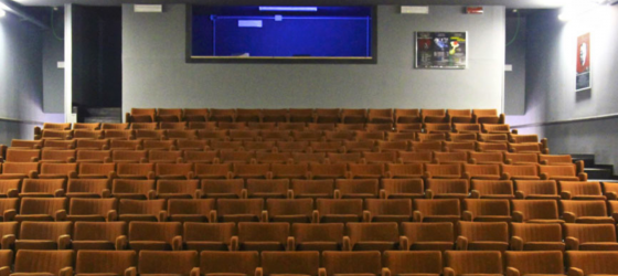 foto platea teatro con poltroncine arancioni e sul fondo la regia