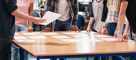 gruppo di donne e giovani intorno a un tavolo con dei fogli a studiare un progetto